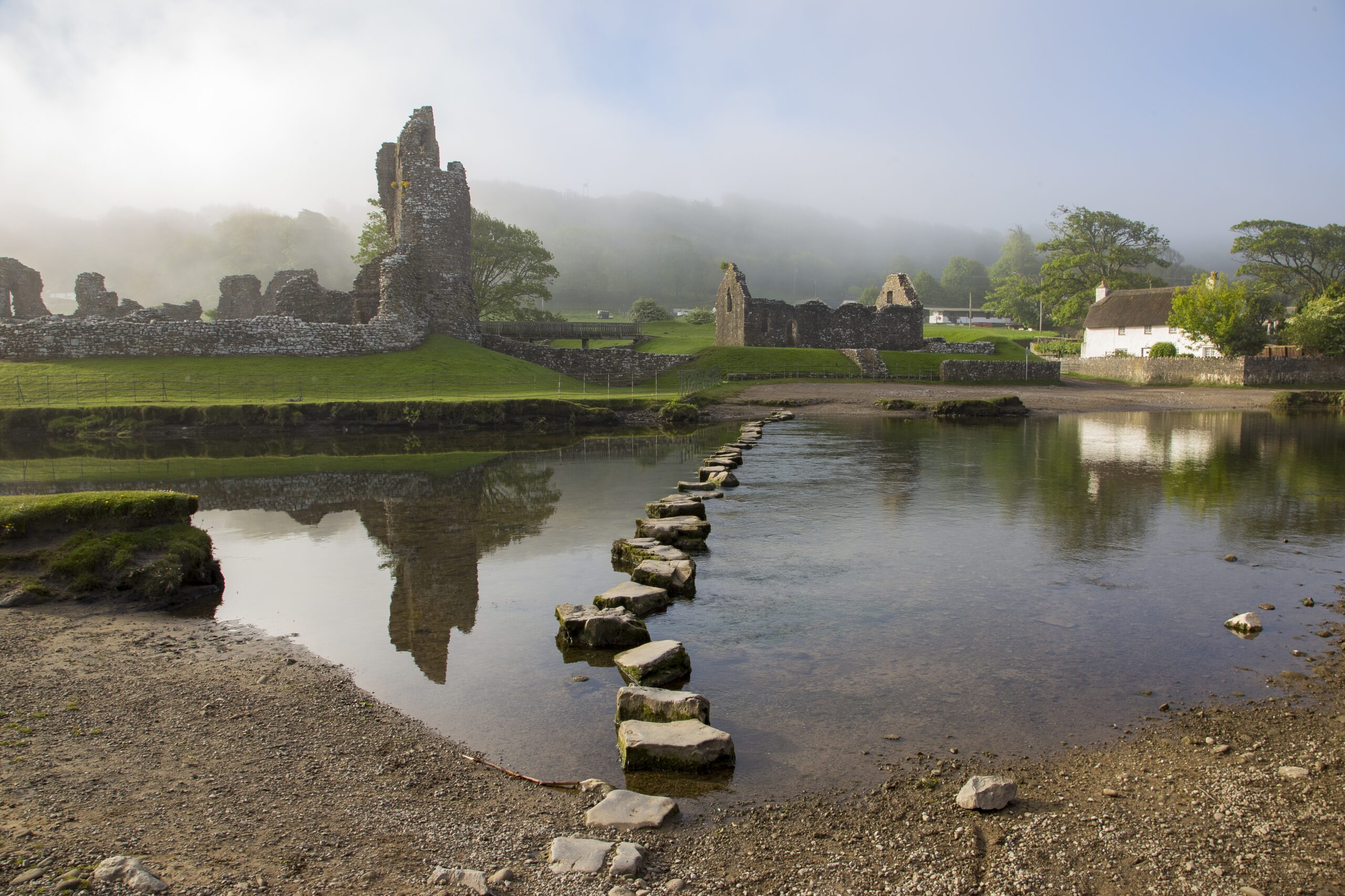 Ogmore Castle ruins with stepping stones across the River Ogmore, Wales.